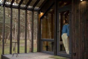 Young woman looks out the window, standing alone in a wooden house on nature. Concept of solitude and rest at countryside